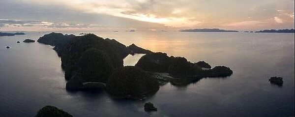 A serene sunrise illuminates the dramatic limestone islands within Raja Ampat, Indonesia. This region is the world's epicenter of marine biodiversity