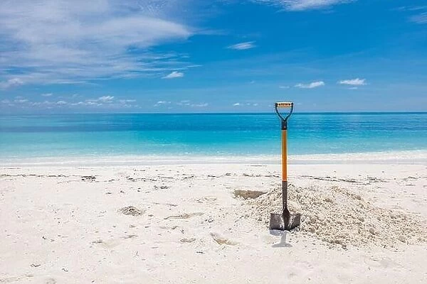 Shovel in Sand at the Beach. Wide angle image of a shovel in the sand on a beach under a partly cloudy blue sky