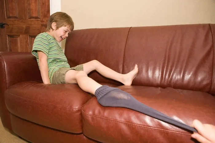 Framed Print : sibling pulling younger brother's sock off on sofa at home Framed Print : sibling pulling younger brother's sock off on sofa at home