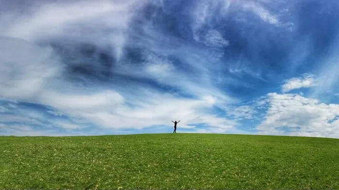 Framed Print : Silhouetted figure with arms held high on horizon of gently rolling grass covered field and blue sky Framed Print : Silhouetted figure with arms held high on horizon of gently rolling grass covered field and blue sky