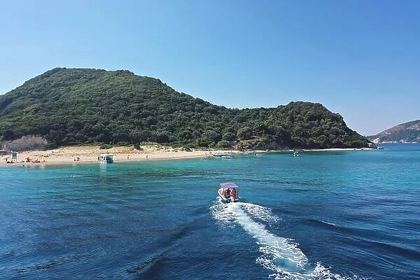 Small boat with tourists heading to iconic small uninhabited island of Marathonisi featuring clear water sandy shore and natural hatchery of Caretta-C