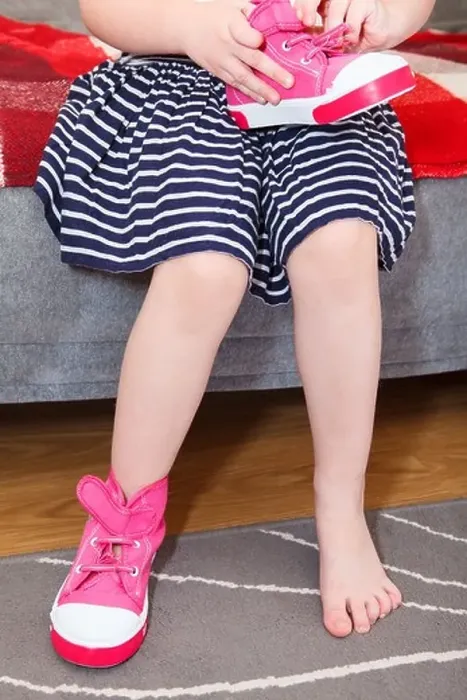 Framed Print : Small girl wearing pink shoes on leg sitting on sofa in domestic room Framed Print : Small girl wearing pink shoes on leg sitting on sofa in domestic room