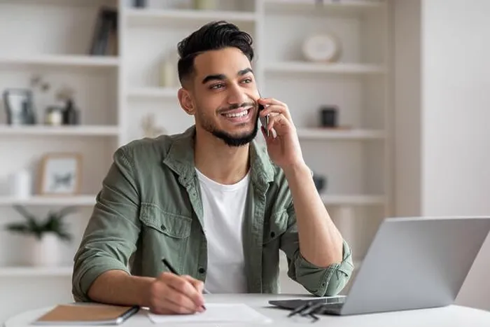 Framed Print : Smiling handsome millennial islamic guy manager with beard speaks by phone at workplace with laptop in home Framed Print : Smiling handsome millennial islamic guy manager with beard speaks by phone at workplace with laptop in home