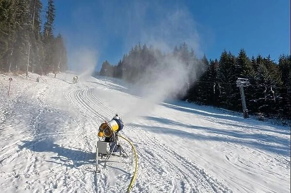 Snow cannon in winter mountains slope. Snow-gun spraying artificial ice crystals. Machine making snow