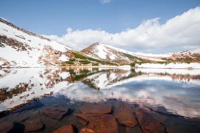 Framed Print : Spring mountain lake with clear water and red stones. Picturesque winter landscape with snowy hills under a blue sky Framed Print : Spring mountain lake with clear water and red stones. Picturesque winter landscape with snowy hills under a blue sky