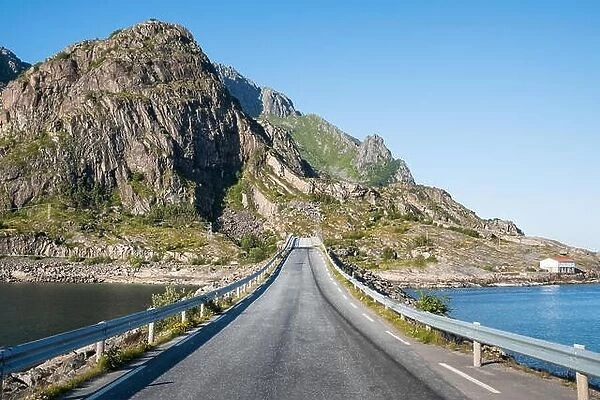 Straight asphalt road with mountain and sea against blue sky in Lofoten, Norway