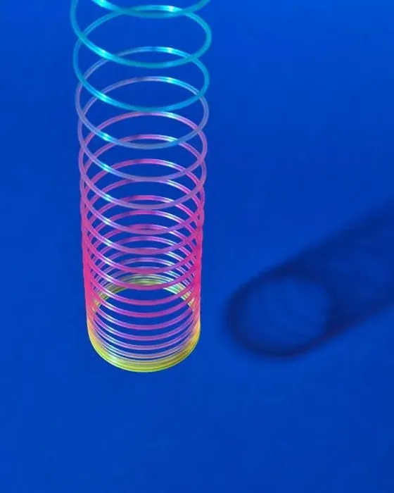 Framed Print : Stretching rainbow plastic slinky toy above blue background with shadows, place for text Framed Print : Stretching rainbow plastic slinky toy above blue background with shadows, place for text
