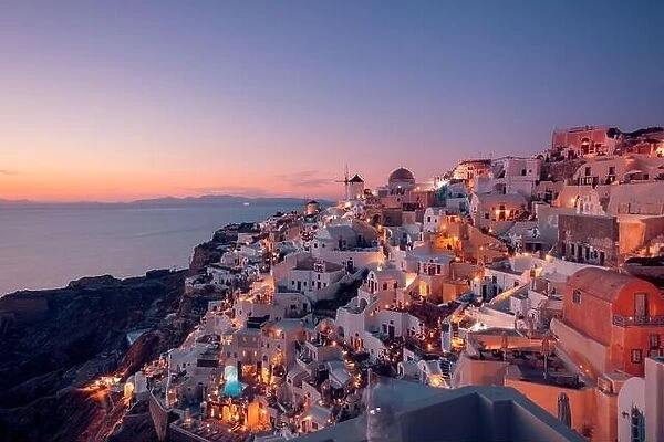 Stunning sunset landscape. Beautiful view of fabulous village of Oia with traditional white houses and windmills in Santorini island at night, Greece