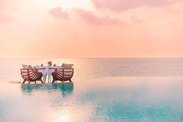 Summer love and romance table setup for a romantic dinner meal with luxury infinity pool reflection chairs under sunset sky and sea in background