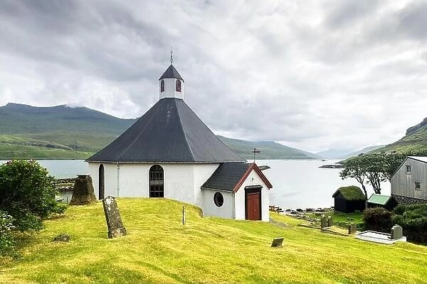 Summer view of traditional church in faroese village. Beauty landscape with foggy fjord and high mountains. Faroe Islands, Denmark
