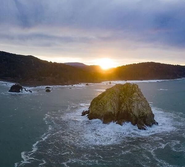 As the sun rises in the east, the cold waters of the Pacific Ocean crash on the rocky Northern California coastline in Klamath