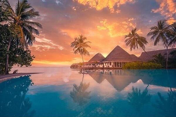 Sunset tourism landscape. Luxurious beach resort with swimming pool reflection beach with palm trees, sunset sky sun rays. Amazing travel background