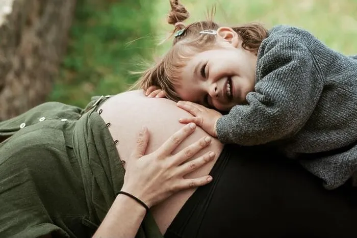 Framed Print : A sweet moment as a young girl with a big smile listens to a pregnant belly, bonding with the unborn sibling outdoors Framed Print : A sweet moment as a young girl with a big smile listens to a pregnant belly, bonding with the unborn sibling outdoors