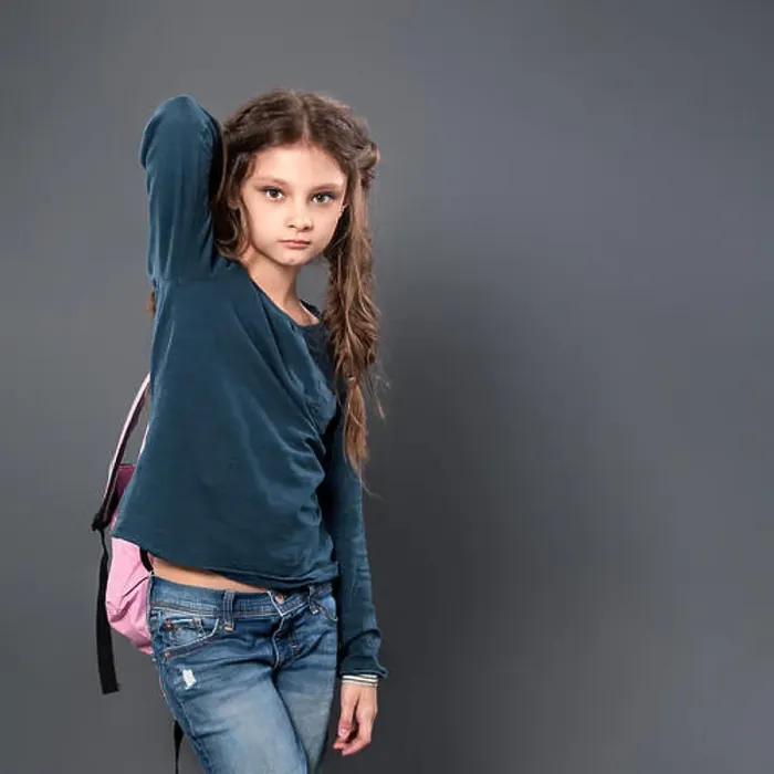 Framed Print : Thinking pupil kid gilr posing in style clothing and holding backpack on grey studio background. Closeup