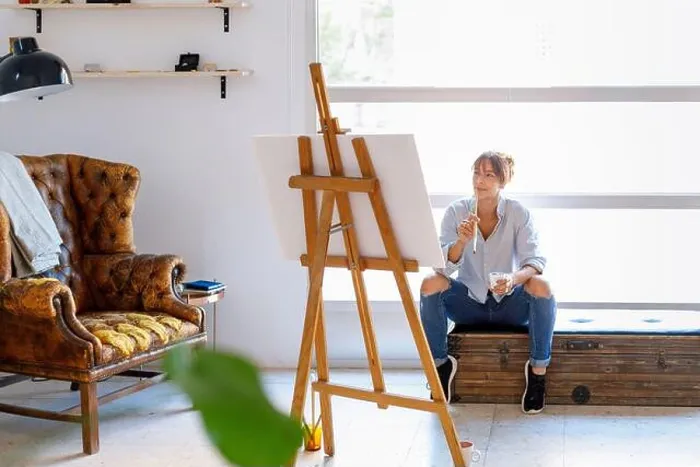 Framed Print : Thoughtful female painter looking at painting while sitting in studio Framed Print : Thoughtful female painter looking at painting while sitting in studio