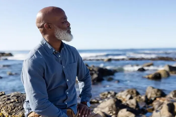 Framed Print : Thoughtful senior african american man sitting on rocks and admiring view at seaside Framed Print : Thoughtful senior african american man sitting on rocks and admiring view at seaside