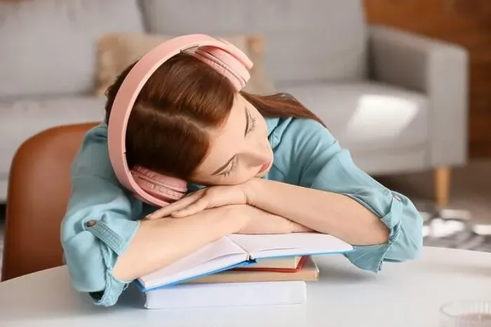 Framed Print : Tired young woman with headphones and books sleeping at table Framed Print : Tired young woman with headphones and books sleeping at table