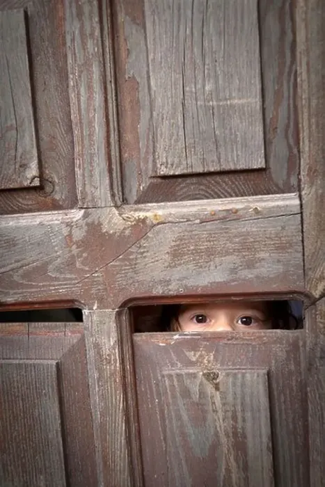 Framed Print : A toddler looks through a small crack in an old wooden door, revealing only her eyes