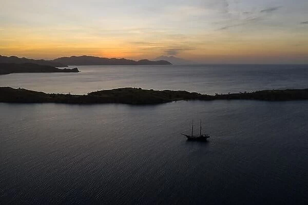 A traditional Pinisi schooner sails at sunset in Komodo National Park, Indonesia. This tropical area is known for its marine biodiversity