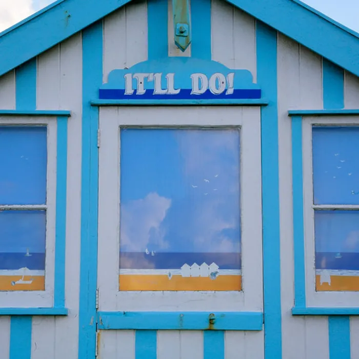 Framed Print : Traditional striped chalet beach hut with seaside scenes painted on windows and 'It'll Do!' name above door Framed Print : Traditional striped chalet beach hut with seaside scenes painted on windows and 'It'll Do!' name above door