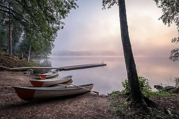 Tranquil beauty morning with row boat and pier at misty summer sunrise in idyllic beach Finland