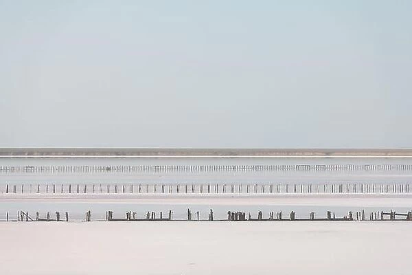 Tranquil minimalist landscape with smooth surface of the pink salt lake with wooden posts with clear sky in sunrise time