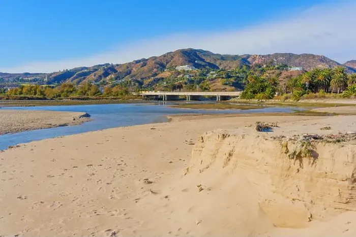 Framed Print : Tranquil scene of a riverbank at Malibu Beach, showcasing soft sandy edges and distant mountains under a clear blue sky Framed Print : Tranquil scene of a riverbank at Malibu Beach, showcasing soft sandy edges and distant mountains under a clear blue sky