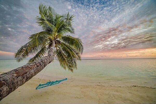 Tranquil summer vacation or holiday landscape. Tropical sunset beach view with palm over calm sea water and swing or hammock. Exotic tranquil nature