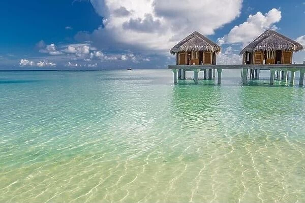 Tropical beach in Maldives with luxury over water bungalows or villas. Amazing sea lagoon with blue sky and clouds. Exotic travel destination