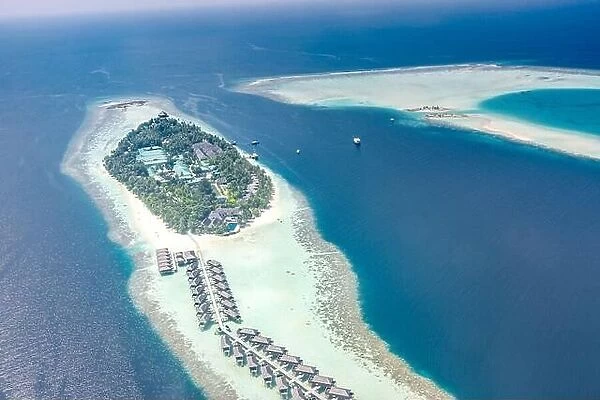 Tropical island at Maldives. Luxury resort from aerial view, over water villas and bungalows over amazing blue sea and lagoon. Luxury summer vacation