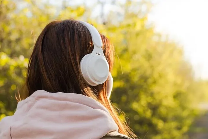 Framed Print : Back view of caucasian young woman listening music with headphones on a sunny day while walking in city park