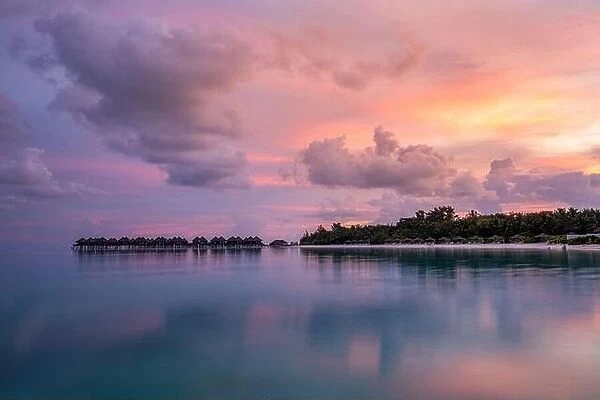 Over water bungalows with amazing lagoon reflection. Colorful sky clouds over tropical island. Summer paradise, luxury landscape. Destination scenic