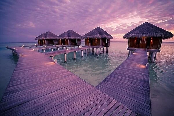 Over water bungalows with steps into amazing green lagoon with coral, Maldives sunset beach
