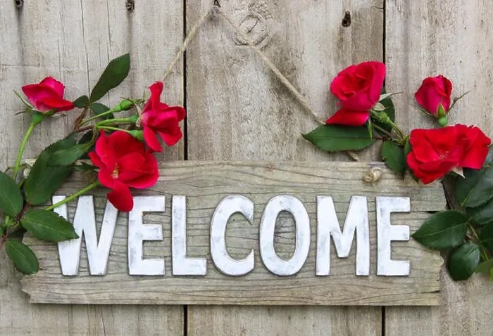 Framed Print : Weathered wood welcome sign hanging on wooden door with flower border of red roses Framed Print : Weathered wood welcome sign hanging on wooden door with flower border of red roses