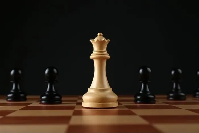 Framed Print : White queen among black pawns on wooden chess board against dark background Framed Print : White queen among black pawns on wooden chess board against dark background
