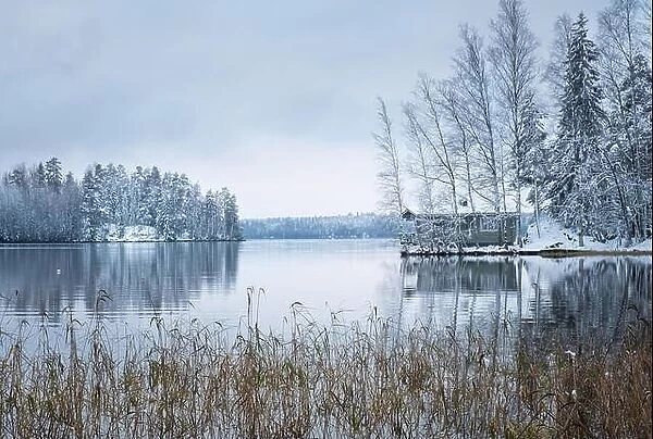 Winter landscape with sauna cottage and peaceful lake at evening in Finland