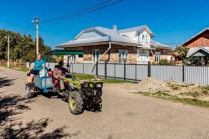 Framed Print : A woman and a man are riding in a cart pulled by a tractor. The cart is on a dirt road in front of a house Framed Print : A woman and a man are riding in a cart pulled by a tractor. The cart is on a dirt road in front of a house