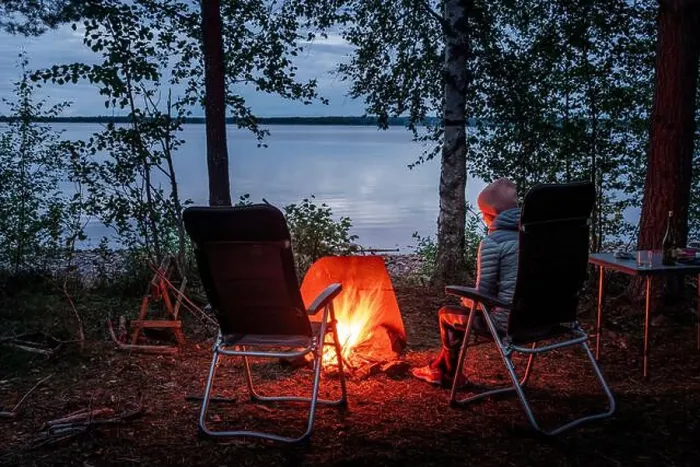 Framed Print : Woman sitting by the campfire in the forest on the banks of Lake Siljan in Dalarna, Sweden