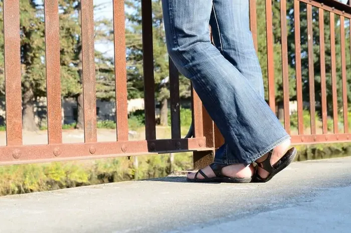 Framed Print : Womans legs and feet standing by a fence wearing jeans and sandals Framed Print : Womans legs and feet standing by a fence wearing jeans and sandals