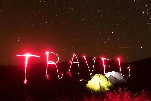Word 2020 written by a red luminous flashlight near lighted from the inside tents against the backdrop of an incredible mountains landscape. Tourism c
