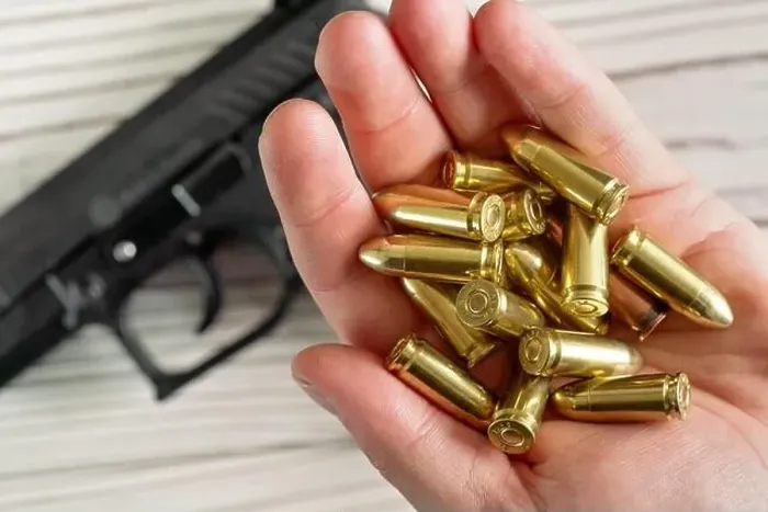Framed Print : Yellow golden coloured bullets held in hand, blurred wooden desk with black gun under Framed Print : Yellow golden coloured bullets held in hand, blurred wooden desk with black gun under