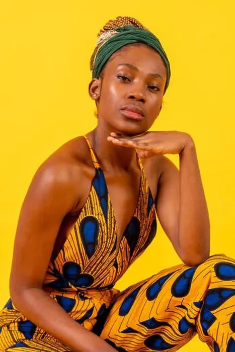 Framed Print : Young african woman with traditional costume on yellow background, sitting looking at camera Framed Print : Young african woman with traditional costume on yellow background, sitting looking at camera