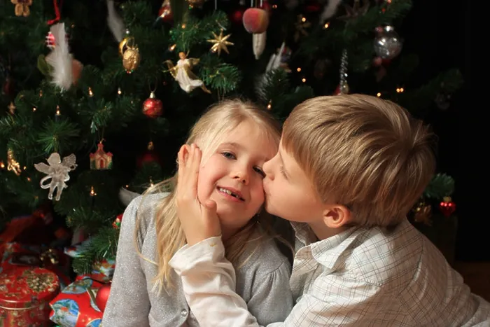 Framed Print : Young boy giving his little sister a kiss in front of a christmas tree with presents below Framed Print : Young boy giving his little sister a kiss in front of a christmas tree with presents below