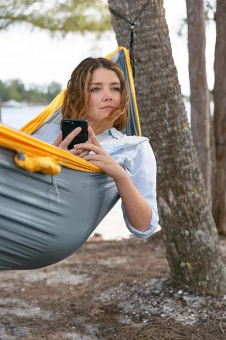 Framed Print : Young brunette woman hold her mobile phone while relaxing on a hammock Framed Print : Young brunette woman hold her mobile phone while relaxing on a hammock