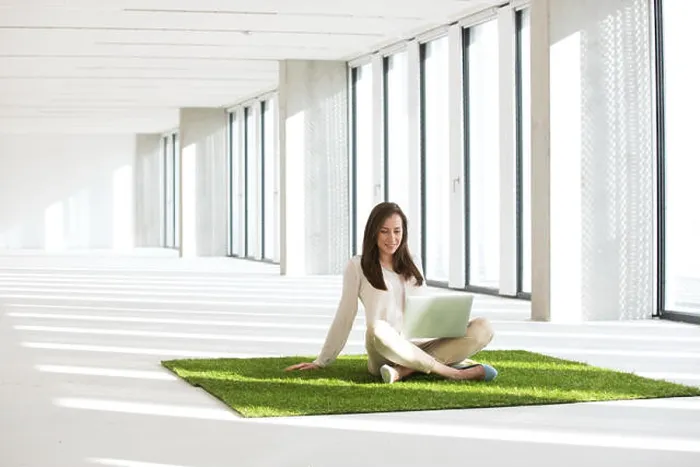 Framed Print : Young businesswoman with laptop sitting on turf in empty office Framed Print : Young businesswoman with laptop sitting on turf in empty office