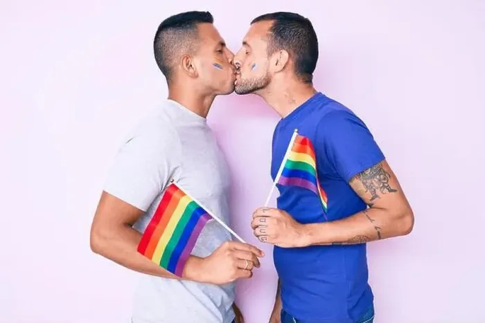 Framed Print : Young couple of gay men together in love holding homosexual pride colorful flag kissing with affection