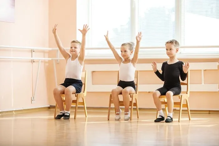 Framed Print : Young dancers playing or doing exercise while sitting on chairs at ballet class Framed Print : Young dancers playing or doing exercise while sitting on chairs at ballet class