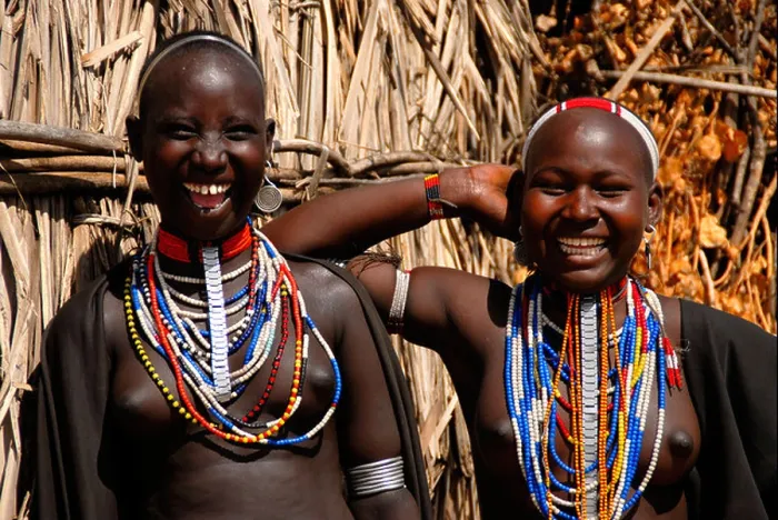 Framed Print : Two young laughing girls of the Arbore people wearing many colourful necklaces in front of a hut Ethiopia