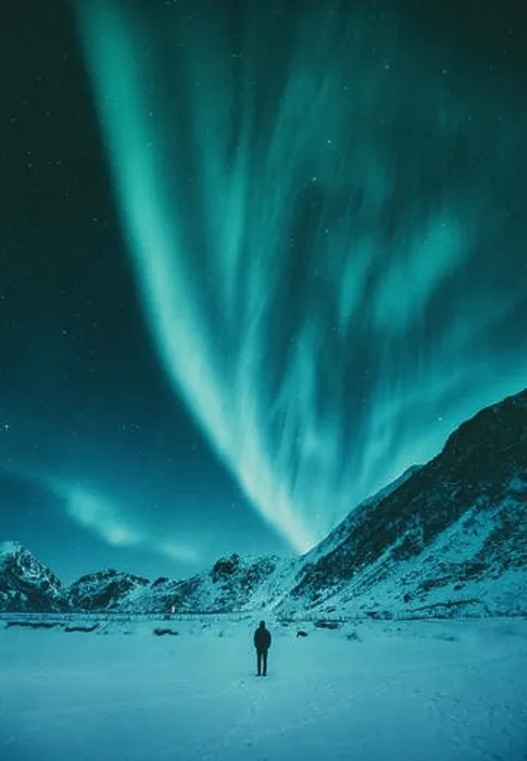 Framed Print : Young man is standing on a remote beach watching the Northern Lights dance above mountains in winter Framed Print : Young man is standing on a remote beach watching the Northern Lights dance above mountains in winter