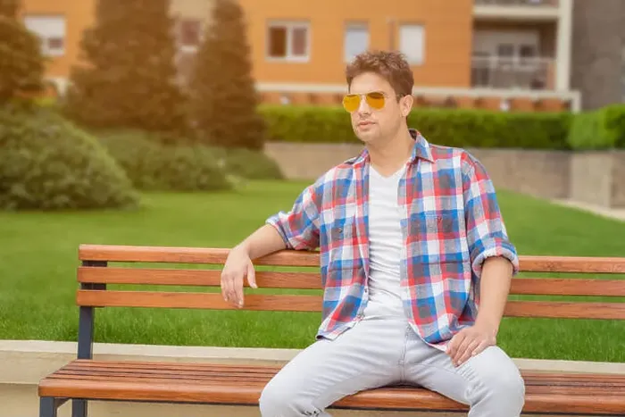 Framed Print : Young modern looking fashionable man posing by sitting on bench in the park Framed Print : Young modern looking fashionable man posing by sitting on bench in the park